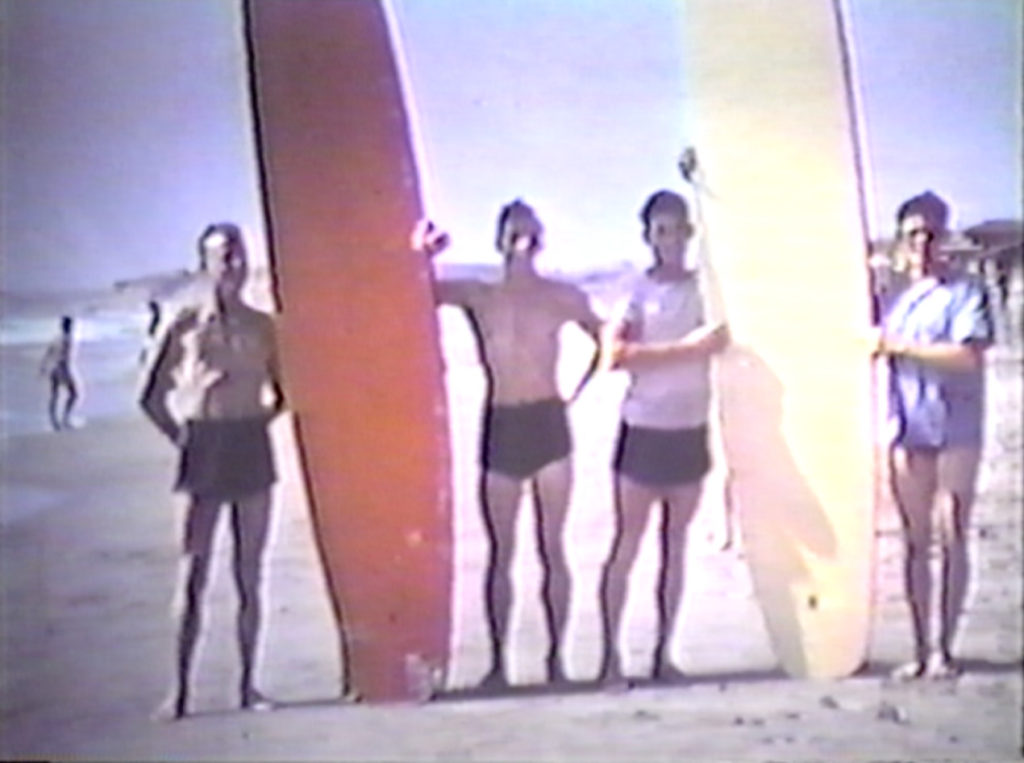 Three boys hold up two surfboards