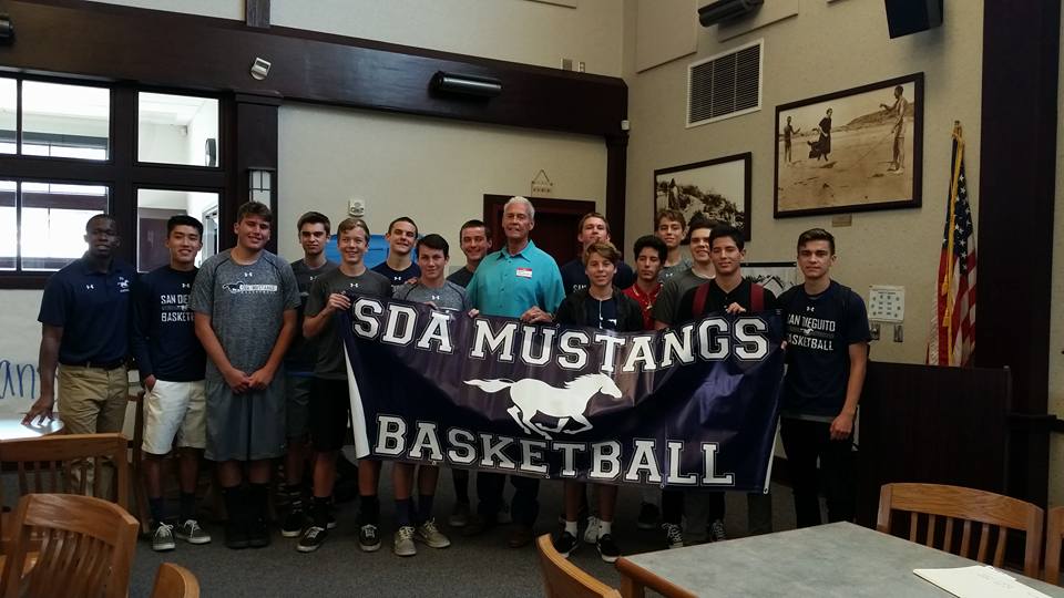 John Fairchild with team members and SDA Mustangs Basketball banner